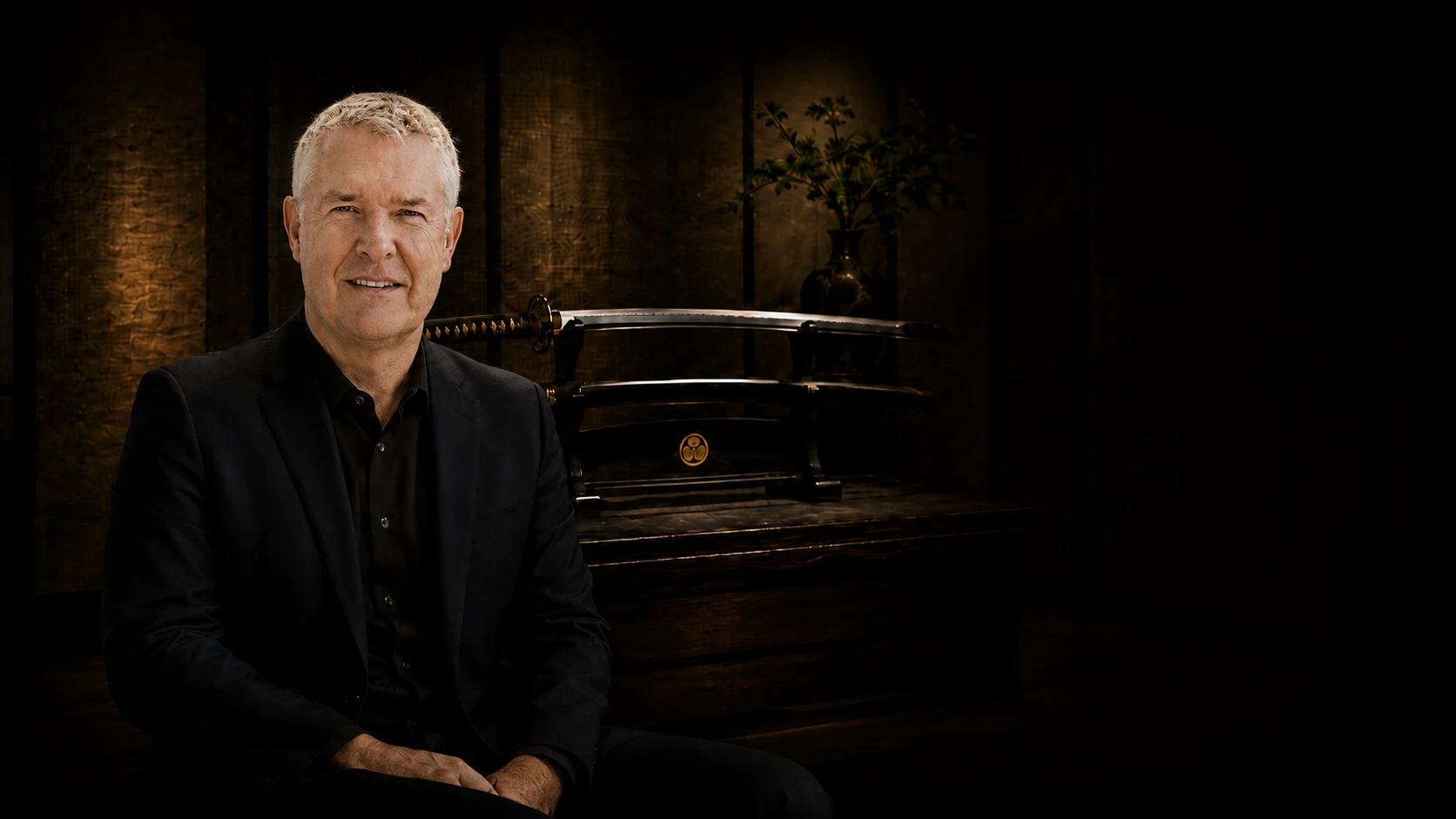 Graeme Somerville-Ryan, seated, with a mounted katana on its stand behind him.